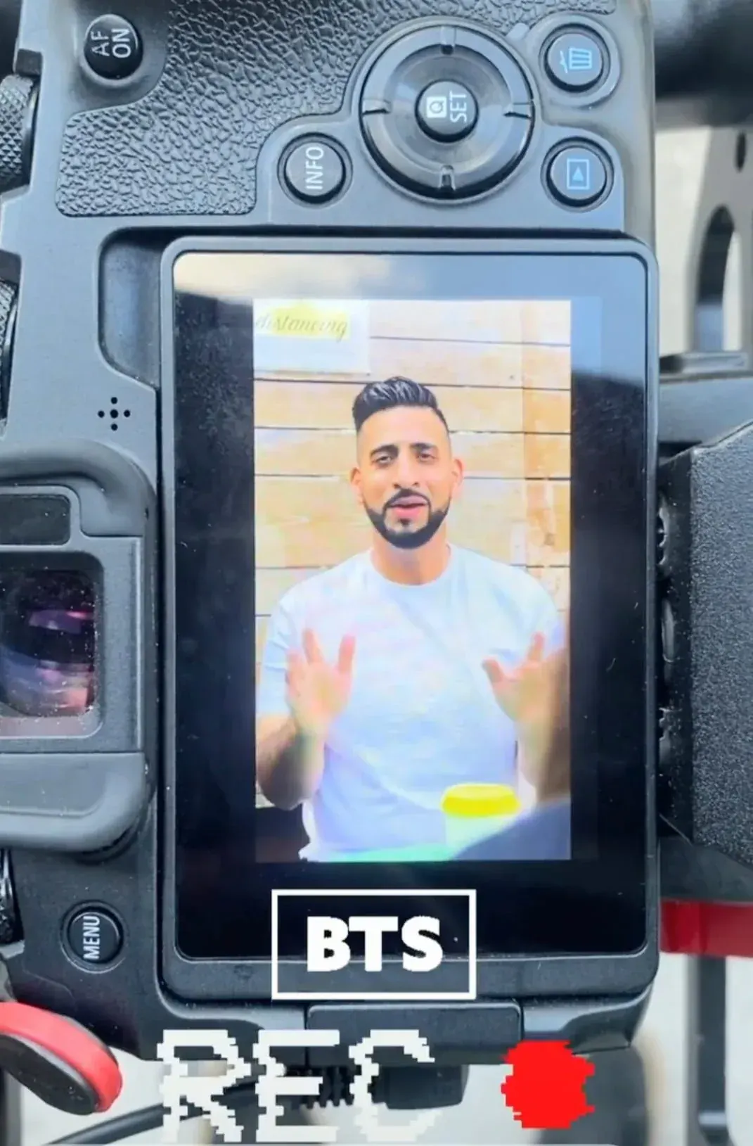 The back screen of a camera on a rig, showing Ali mid-take against a pale yellow wall